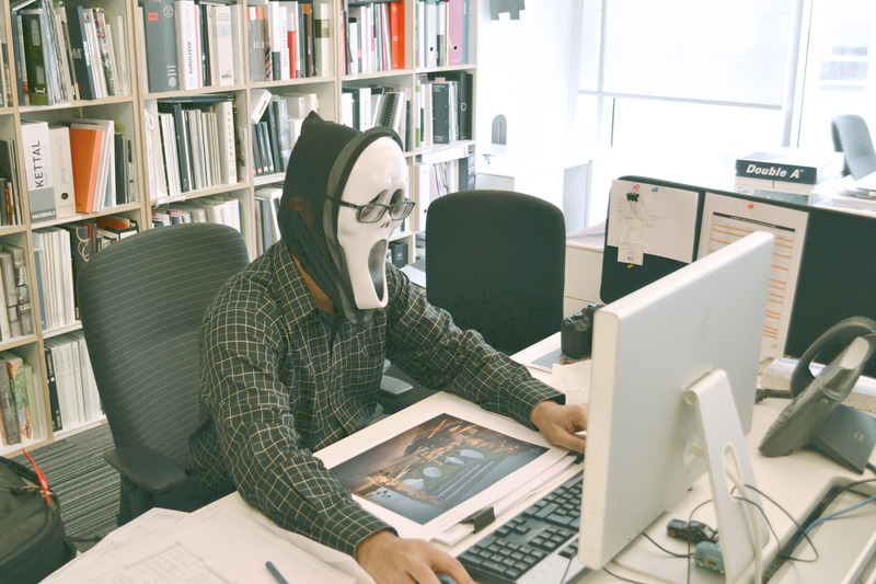 A Person Wearing Scream Mask and Black Dress Shirt While Facing Computer Table during Daytime